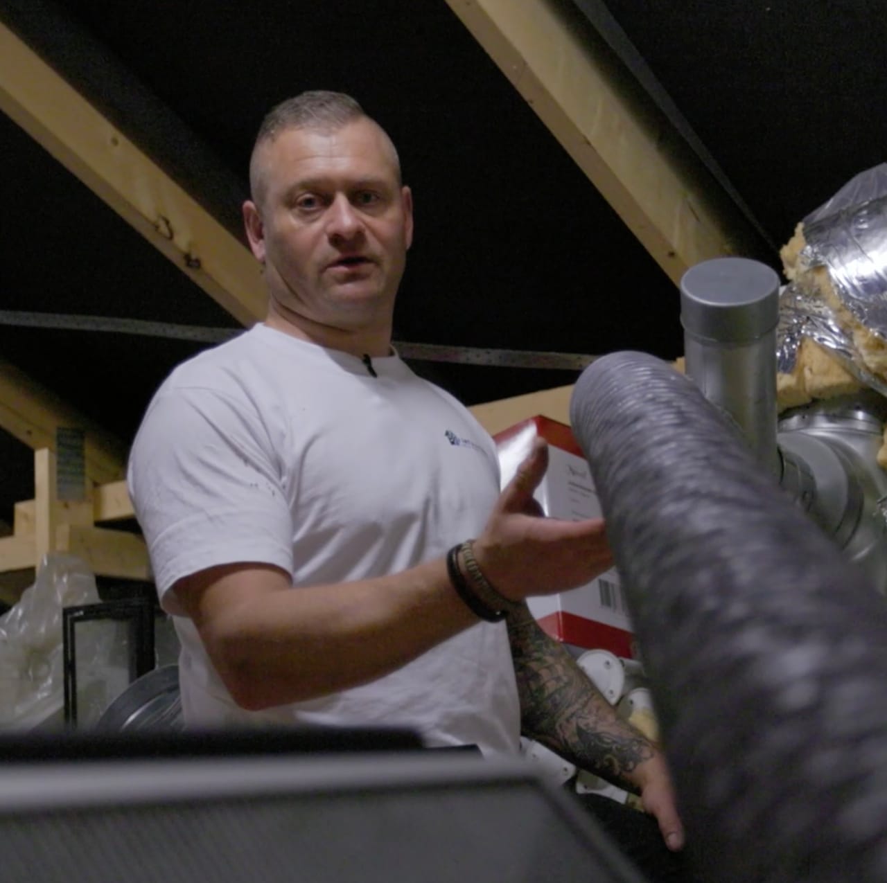 Andi fra Ventipartner ved et ventilationsaggregat og kanaler på et loft